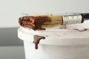 Drops of brown paint flow down from a brush.